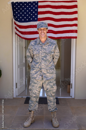 Full length portrait of smiling caucasian army soldier standing against usa flag at entrance