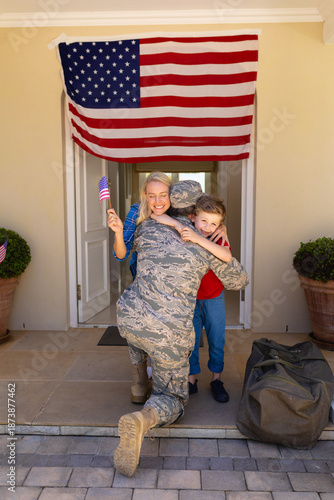 Caucasian woman and son with usa flag hugging army soldier on his return at the entrance