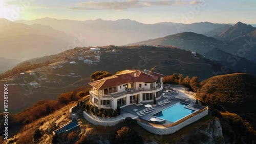 Luxury villa aerial view. A natural landscape with a building on a hill with a swimming pool overlooking the sunset, surrounded by sky, mountains, clouds, and light
