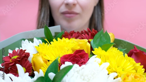 Young woman holding bouquet of flowers covering her face on pink background.