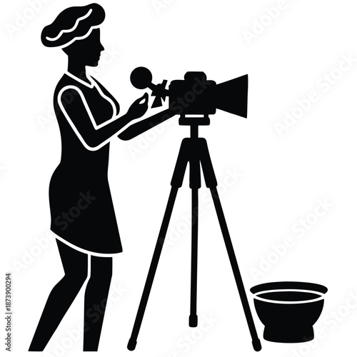 Silhouette of a person in chef hat operating a video camera on tripod with a bowl