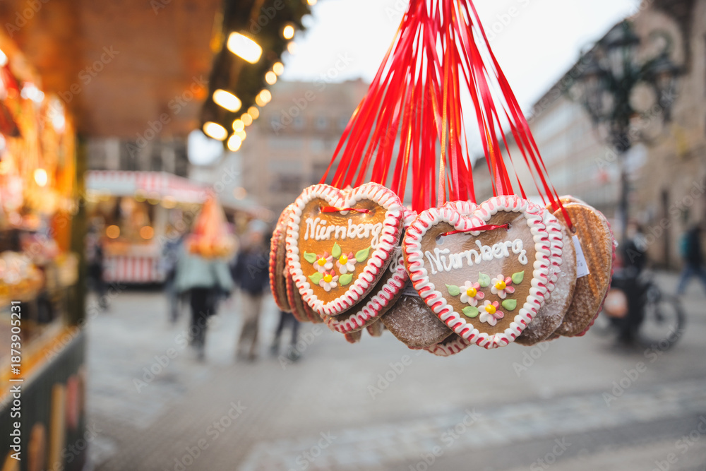 Fototapeta premium Heart shaped gingerbread cookies with nurnberg text and floral icing designs hanging from red ribbons, selling at a traditional german christmas market