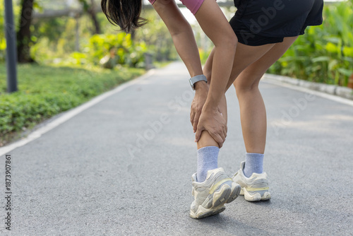 Obraz na płótnie Close-up of female runner holding her lower leg in pain during outdoor workout, representing sports injury, leg cramp or muscle strain, often experienced in fitness and running activities