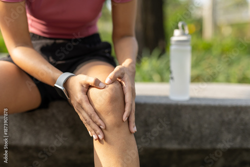 Obraz na płótnie Close-up of women sitting on bench holding her knee in pain after exercise, representing workout injury, joint discomfort and recovery in outdoor fitness activity