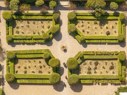 Aerial view of geometrically precise gardens with manicured hedges casting long shadows, contrasting with the earthy tones of the pathways and the central fountain, Pienza, Tuscany, Italy.