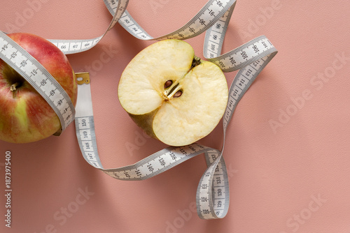 Diet, weight loss concept, healthy eating. Cut red apple wrapped with white measuring tape on pink background as a symbol of weight loss and diet. Soft focus.