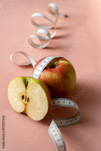 Diet, weight loss concept, healthy eating. Cut red apple wrapped with white measuring tape on pink background as a symbol of weight loss and diet. Soft focus.