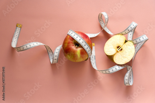 Diet, weight loss concept, healthy eating. Cut red apple wrapped with white measuring tape on pink background as a symbol of weight loss and diet.
