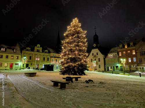 winterlicher Marktplatz mit Weihnachtsbaum und Schnee im Lichterschmuck bei Nacht