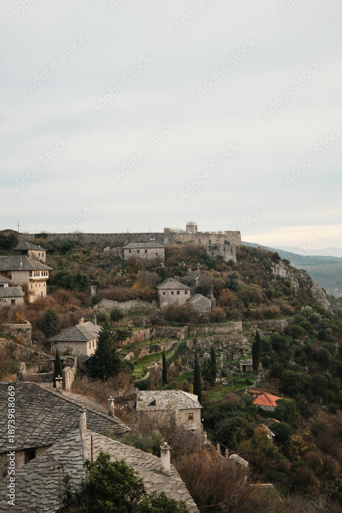 Obraz premium Wide view of Pocitelj Fortress with stone houses and terraced gardens on the hillside above the Neretva River, showing preserved medieval village architecture in Bosnia and Herzegovina.