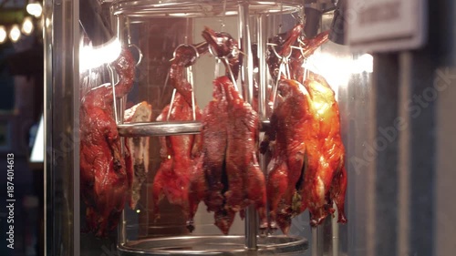 Roasted Peking ducks with glistening skins hanging on rotary roaster oven in Chinese restaurant, invoking culinary traditions