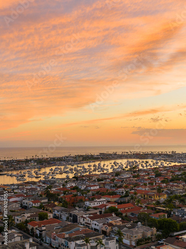 Aerial view of rooftops and harbor reflecting the fiery sunset hues, Newport Beach, California, United States.