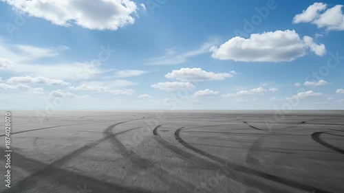 Wallpaper Mural A wide, expansive shot captures an immense, flat ground covered in countless dark tire tracks, stretching towards a distant, clear horizon. Above, a bright blue sky is adorned with scattered, fluffy w Torontodigital.ca