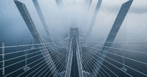 Cinematic drone view looks down on geometric suspension bridge cables and supports crossing a foggy river at cool grey dawn