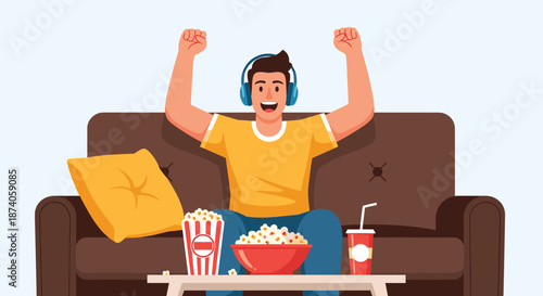 Excited man wearing headphones cheering on a brown sofa with popcorn and a drink while watching a sports game or movie at home.
