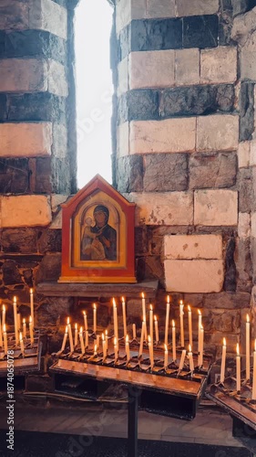 Interior view of a very old church with lit candles placed as offerings, symbolizing faith, devotion, and prayer. The warm candlelight illuminates religious figures and sacred spaces