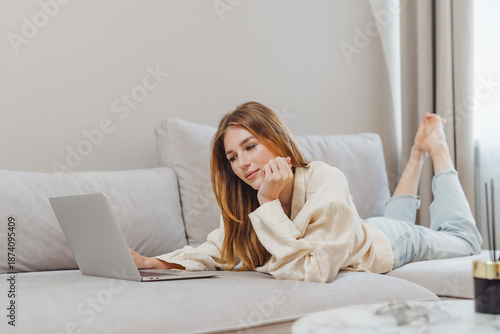 Freelance student working from home on a laptop while relaxing on a couch in the afternoon light
