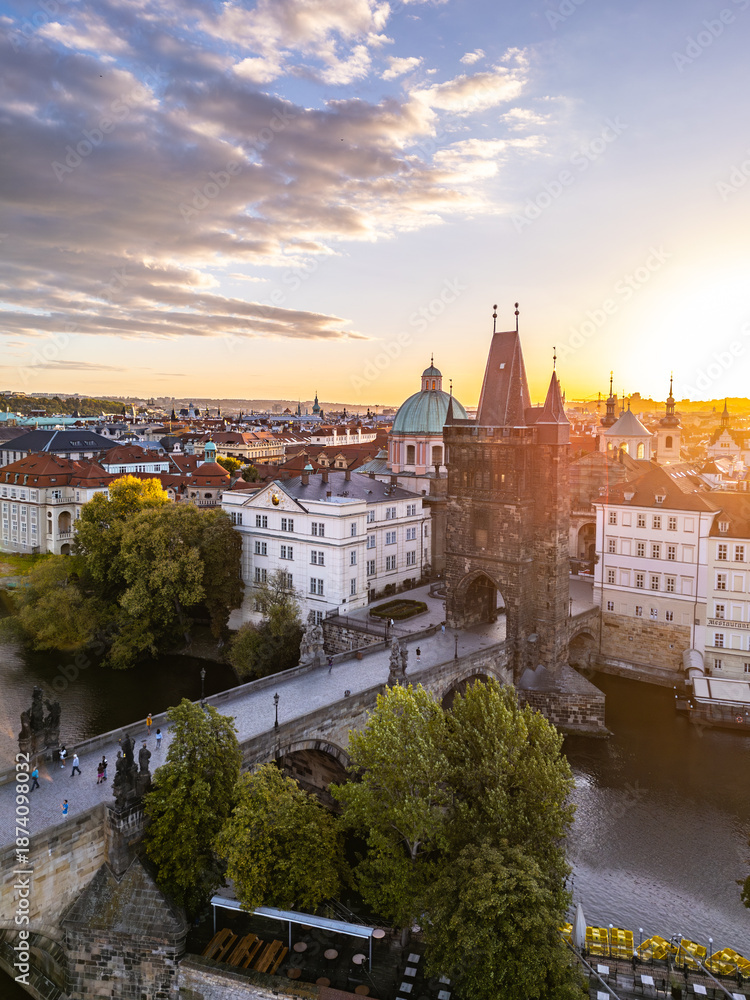 Obraz premium Sunset casts a warm glow on the Old Town Bridge Tower at Charles Bridge in Prague. The scenic view highlights the historic architecture and the Vltava River below, creating a charming atmosphere.