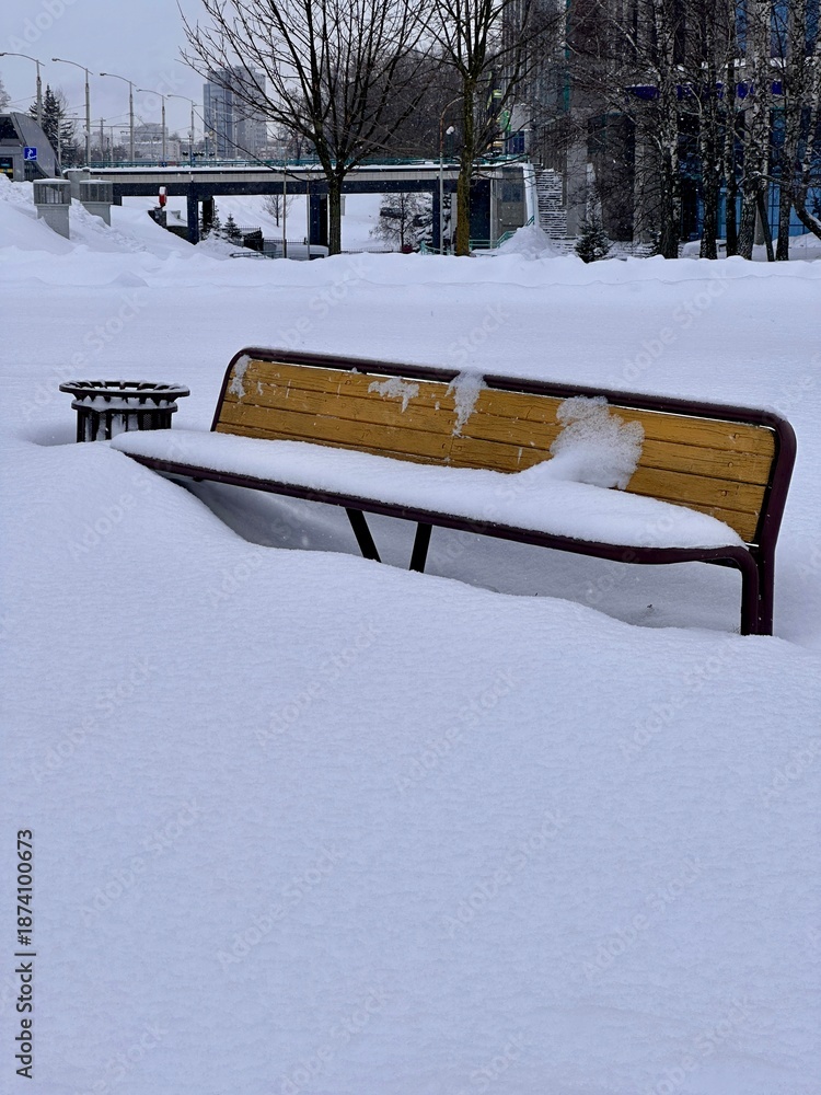 Fototapeta premium Snow-covered bench in the city. European winter, snowfall, natural disasters.