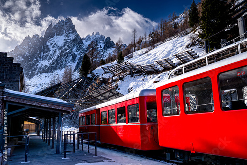 Red Montenvers Mer de Glace train with people in French Alps stands at train station overlooking high mountains, Chamonix-Mont-Blanc, France. Tourist attraction in the Alps winter.