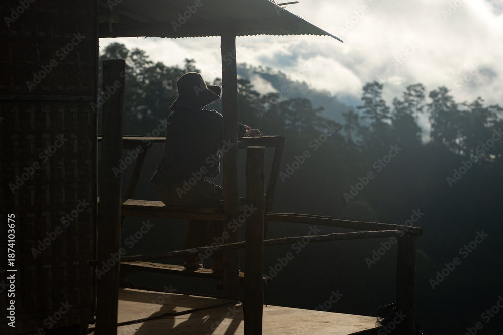 Fototapeta premium Silhouette of a person resting on a wooden balcony overlooking misty mountains