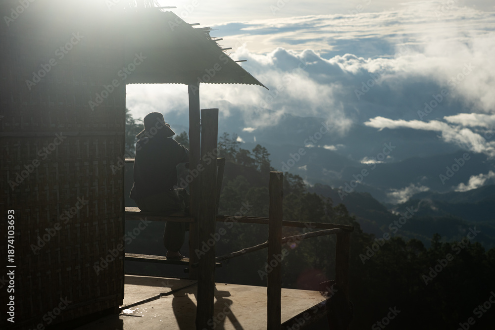 Fototapeta premium Silhouette of a person resting on a wooden balcony overlooking misty mountains