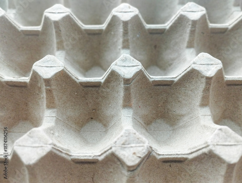 A top-down, close-up view of an empty grey molded pulp egg tray, showing a repetitive geometric pattern and textured paper surface.
