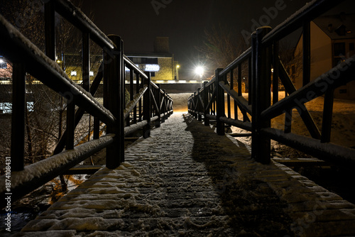 Backlit wooden bridge at night with snow and warm lighting