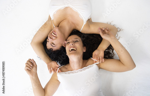 Two sexy brunette, women, curly hair, lie on the floor, laughing joyfully, their heads resting together, radiates warmth, happiness, carefree bond of friendship, full of positive energy