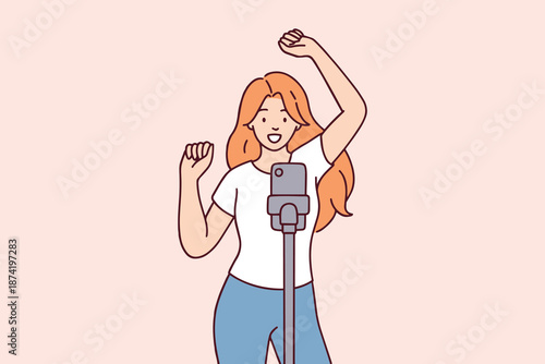 Joyful girl recording a dance for social media using her phone on a tripod. Concept of modern digital creation, vlogging, and fun active lifestyle.