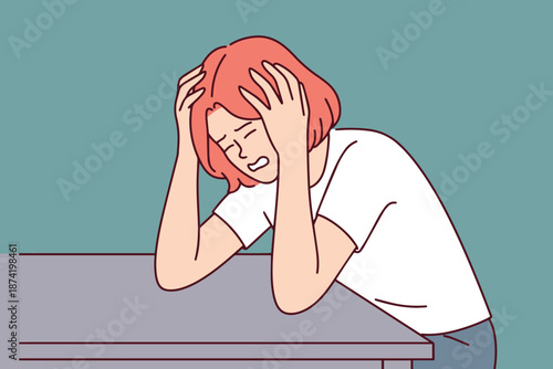 Young woman in distress sitting at table with head in hands. Concept of professional burnout or chronic health problems causing severe headache and mental exhaustion