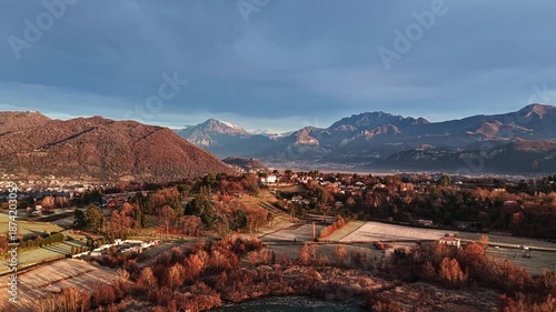Aerial drone shot pulling back to reveal a frozen lake surrounded by winter countryside and distant mountains, calm and cinematic landscape at sunrise.