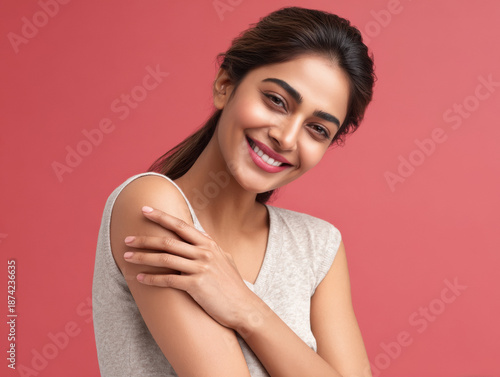 indian woman smiling and touching his shoulder on pink background