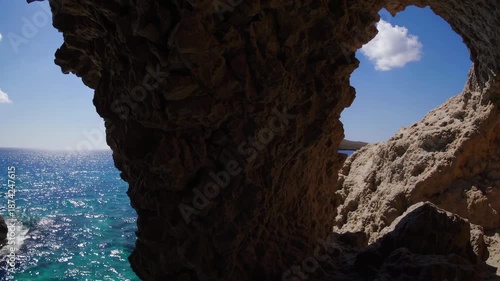Breathtaking coastal scenery featuring a rocky cave opening overlooking a vibrant blue sea. sunlight shimmers on the waves, and a distant cliff creates a picturesque horizon. the serene scene embodies