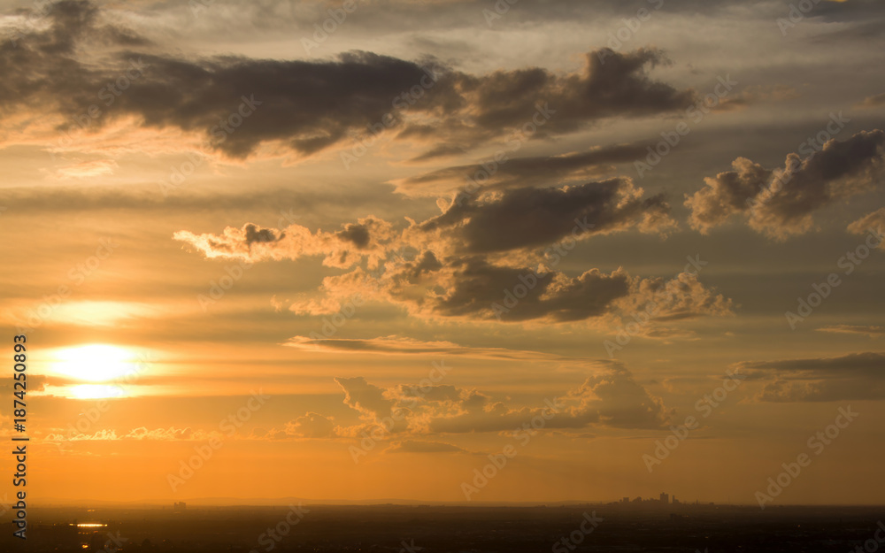 Obraz premium The sun sets behind a vast landscape with a predominantly orange sky filled with scattered clouds during a serene moment of natural beauty at dusk