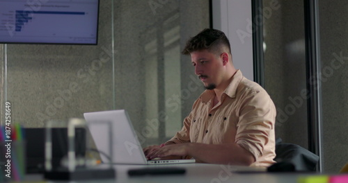 Photos Young male employee types focused on laptop at modern office desk during quiet s