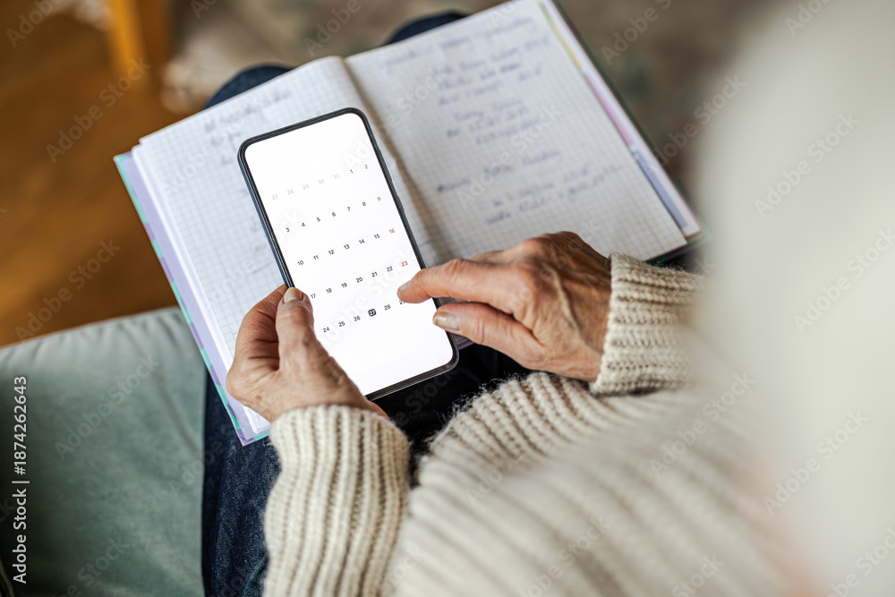 Naklejka premium Senior woman using written notes and her mobile phone