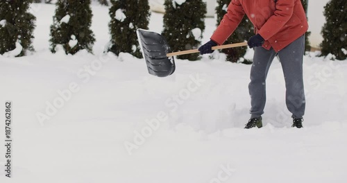 Young man cleans snow with a shovel after snowfall background of the house in winter.