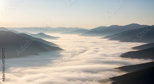 Aerial view of mountain peaks emerging from a valley of clouds, bathed in soft morning light, creating a serene, misty scene