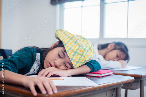 Quadro su tela Tired cute Asian schoolgirl sleeping on wooden desk in classroom