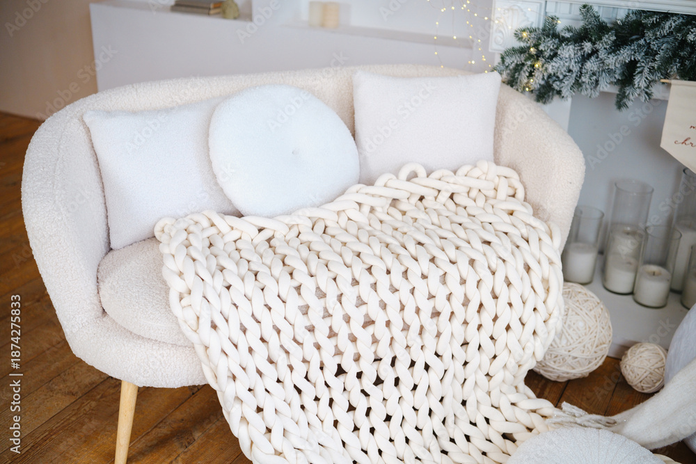 Fototapeta premium Cozy cream sofa with knit blanket and pillows, warm winter home interior scene.