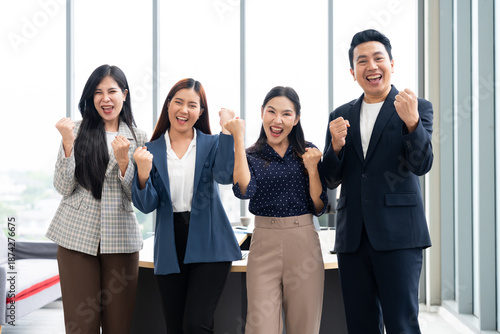 Happy Asian business team celebrating success in office, raising arms and cheering. Professional colleagues achieving goals, corporate win, and teamwork victory concept in modern workspace