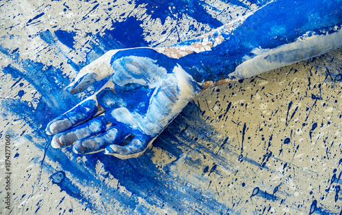 Paint covered human hand resting on abstract blue splattered surface, expressive body art detail symbolizing creativity, touch, process and raw artistic action in contemporary art