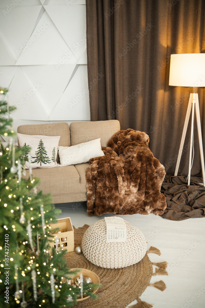 Fototapeta premium Cozy living room with decorated Christmas tree, plush sofa and warm blanket, natural light