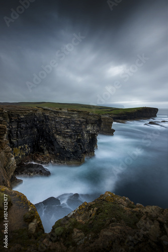 View of rugged cliffs meet the turbulent, foamy sea under a foreboding sky, a silent drama unfolding in the Scottish landscape, Kirkwall, Scotland, United Kingdom.