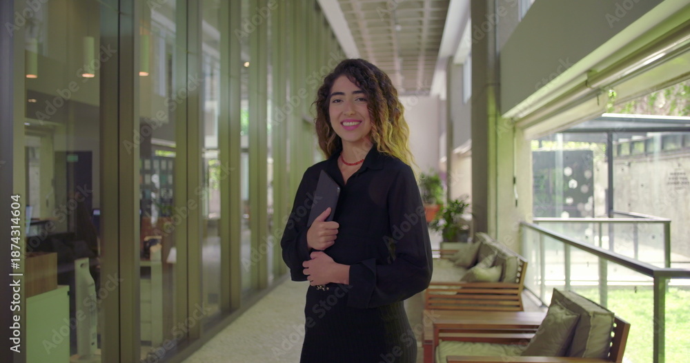 Fototapeta premium Young woman smiling in full body portrait while holding tablet, standing in office hallway, confident and approachable in modern business environment