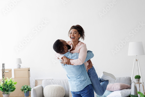 Fotografi Happy couple moving at bought house, husband lifts up beloved wife, family begin new life at first dwelling, copy space