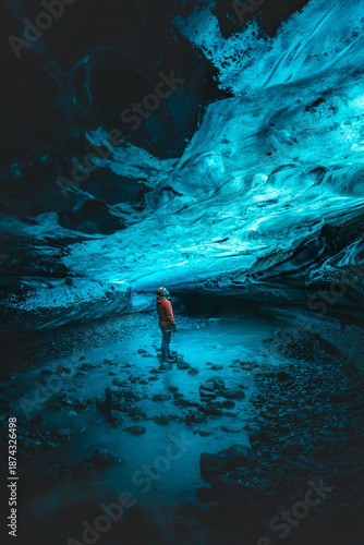 View of a person standing in a pool of water inside an ice cave, with blue ice formations overhead, creating a surreal and ethereal atmosphere, VatnajÃ¶kull National Park, South Iceland, Iceland.