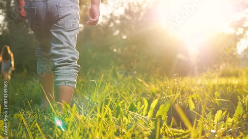 Little contented child joyfully dashes barefoot on grass in park during warm weather. In meadow gleeful child boy sprints shoeless across lush greenery. Happy kid runs cheerfully across grass