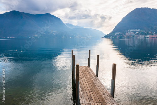 Lugano lake with Alps mountains in Lugano, Switzerland. Wooden pier on the shore of lake.